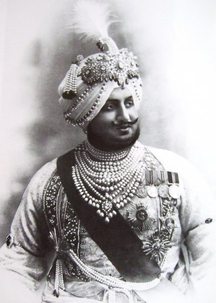 Maharaja Bhupendra Singh of Patiala. 1911. Wears an aigrette or Sarpech by Cartier and various other turban ornaments. While the front of aigrette is set with diamonds, rubies and emeralds, the back shows the intricacy of craftsmanship with foliate motifs of red, green and blue enamel. He also wears a necklace of fourteen strands of natural pearls.