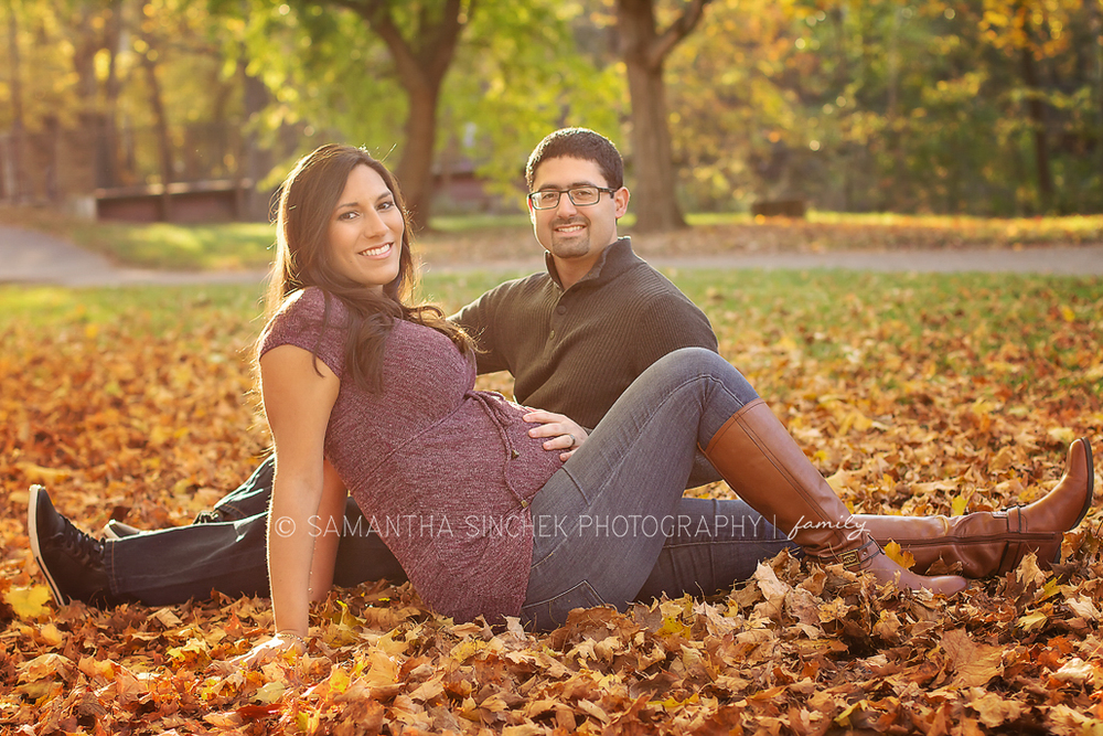 parents to be sit in the fall leaves at a maternity session at sharon woods ohio