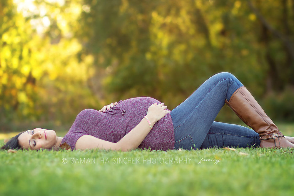 maternity client lays down in the grass and hold belly during cincinnati maternity session