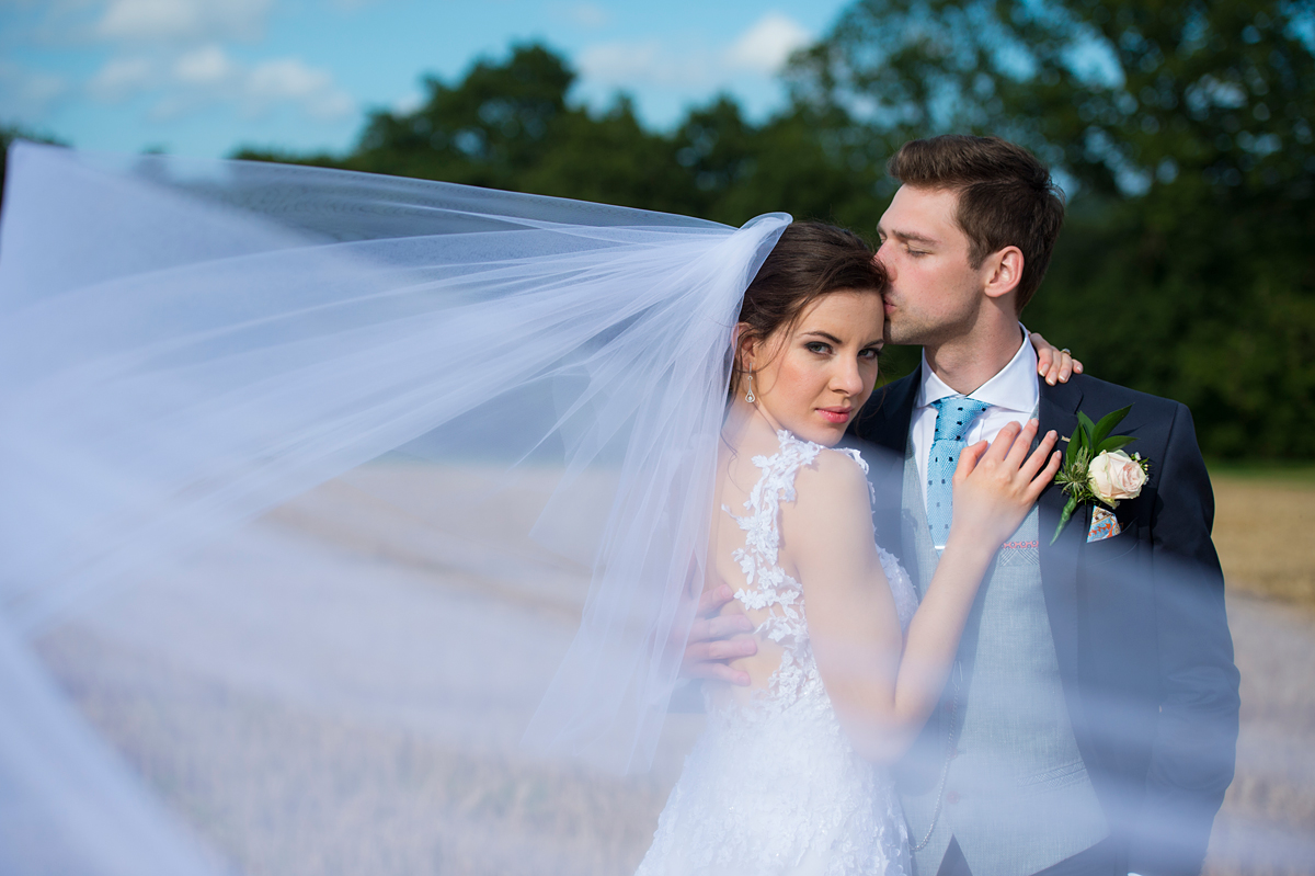 photograph of a bride a groom in stubble field with veil blowing in the breeze