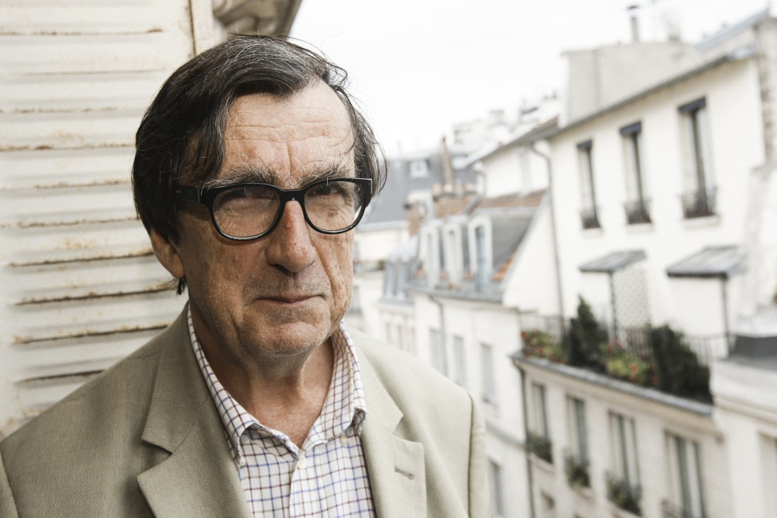 A photograph of Bruno Latour against an urban residential background