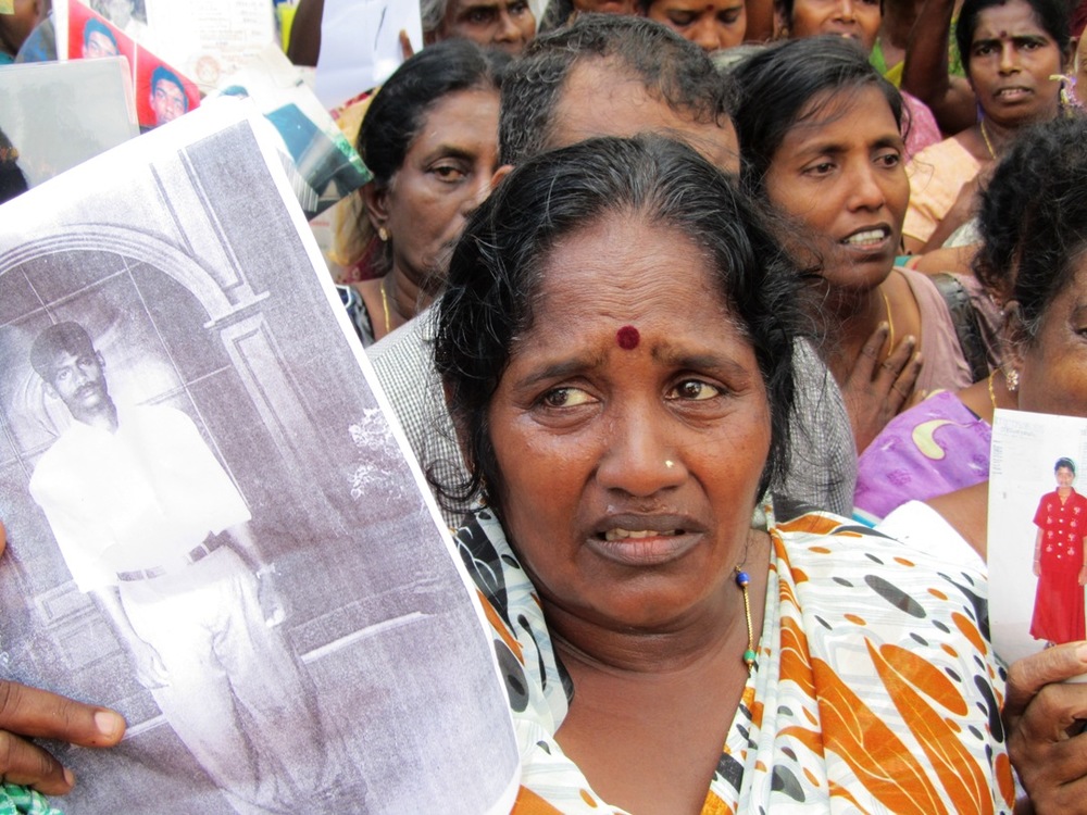 a tamil woman tearfully holds up photographs of her disappeared loved ones at a demonstration in jaffna in december 2011. image courtesy of tamil guardian.