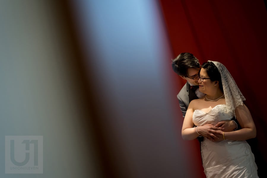 Groom hugging bride from behind in front of a red wall in Ottawa