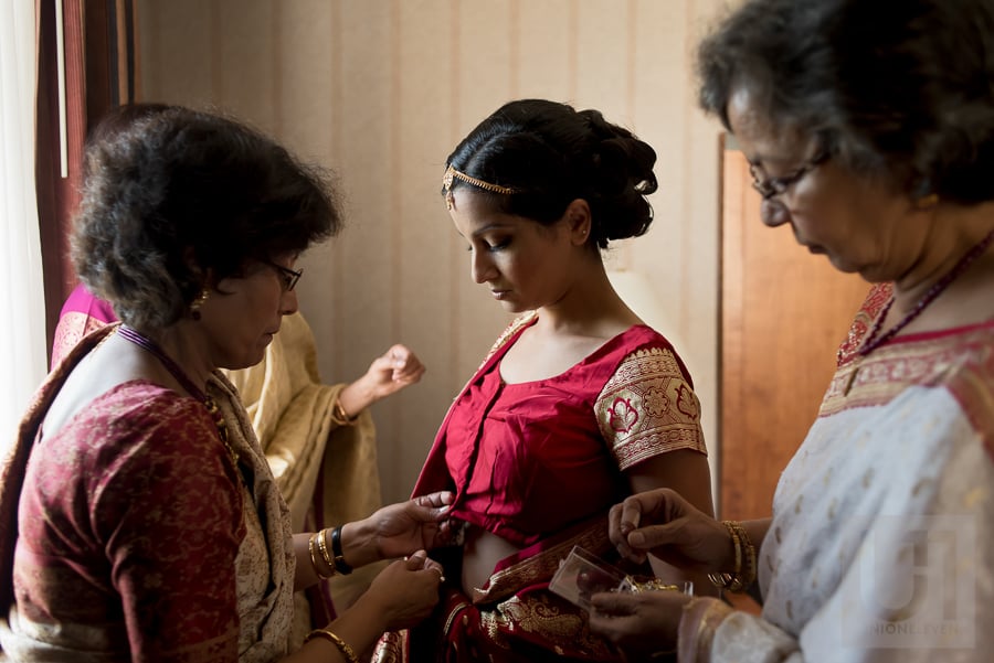 bride in traditional Hindu outfit being dressed by mother and family members