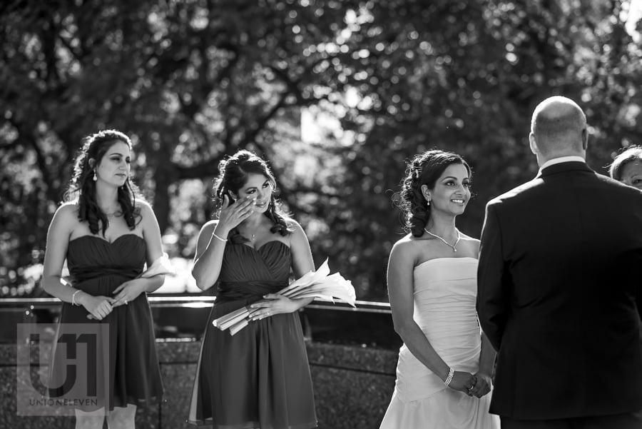 bride looking at groom lovingly during wedding ceremony, while bridesmaid wipes her own tears in the background 