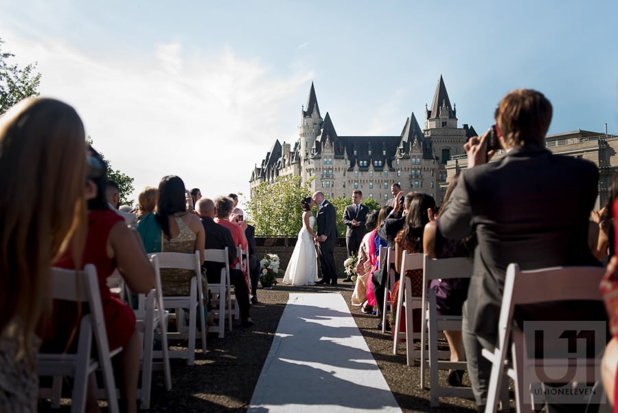 bride and groom sharing first kiss during rooftop wedding ceremony at the National Arts Centre in Ottawa, with the Chateau Laurier in the background