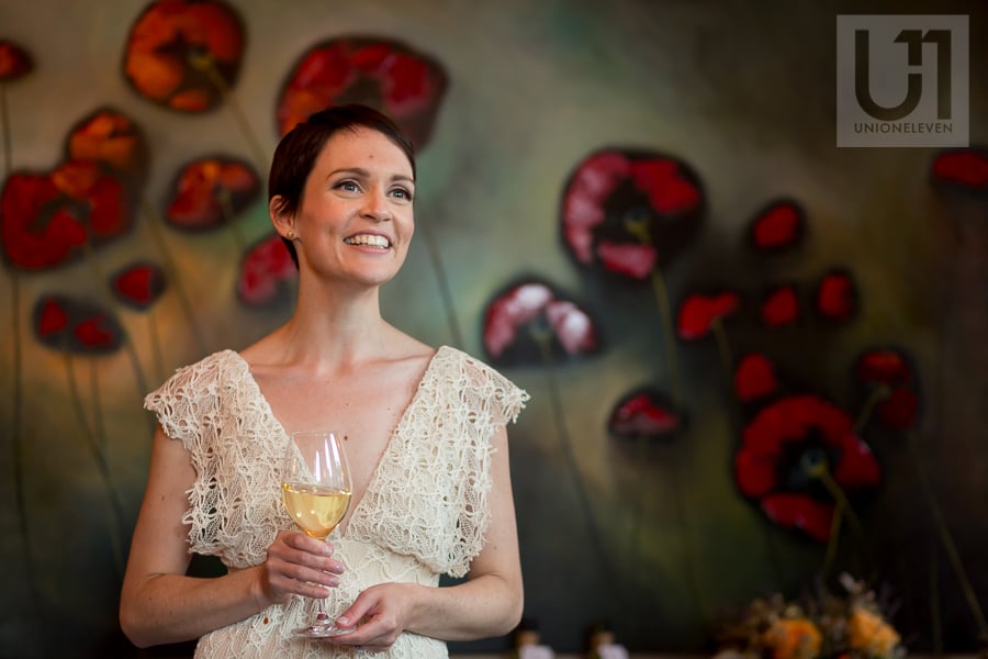 Bride holding glass of white wine in front of large painting of poppies at Beckta in Ottawa.