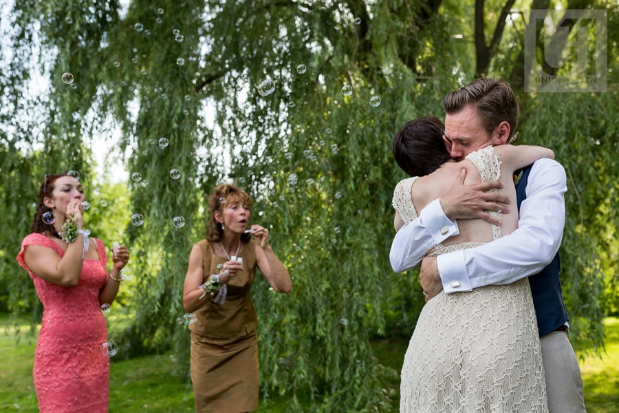 Bride and groom hugging while guests blow bubbles at them at the Arboretum in Ottawa.