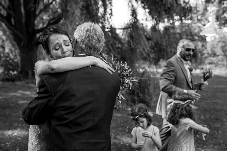 Black and white image of bride hugging man after wedding ceremony, crying.