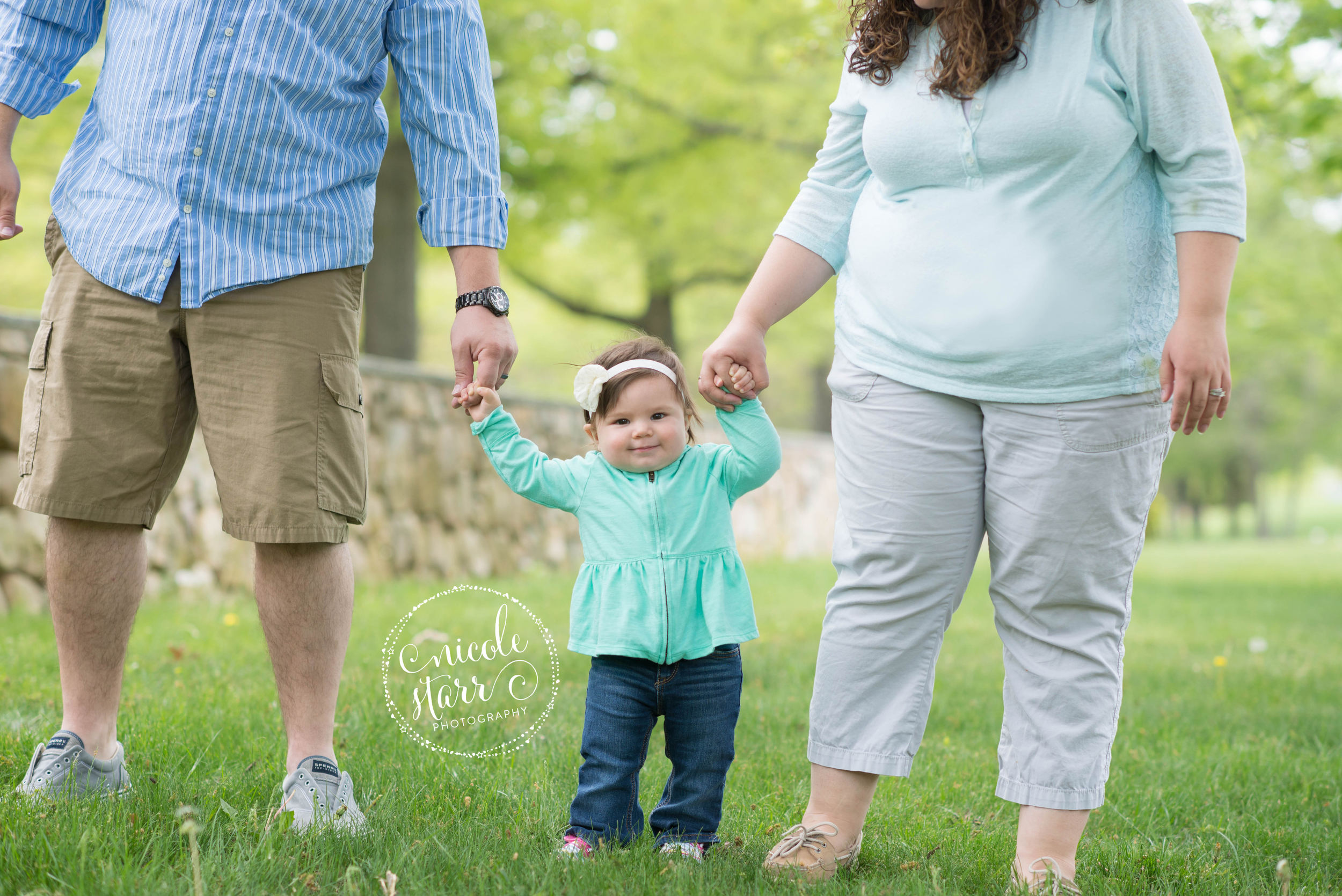 baby taking first steps in family photo with mom and dad