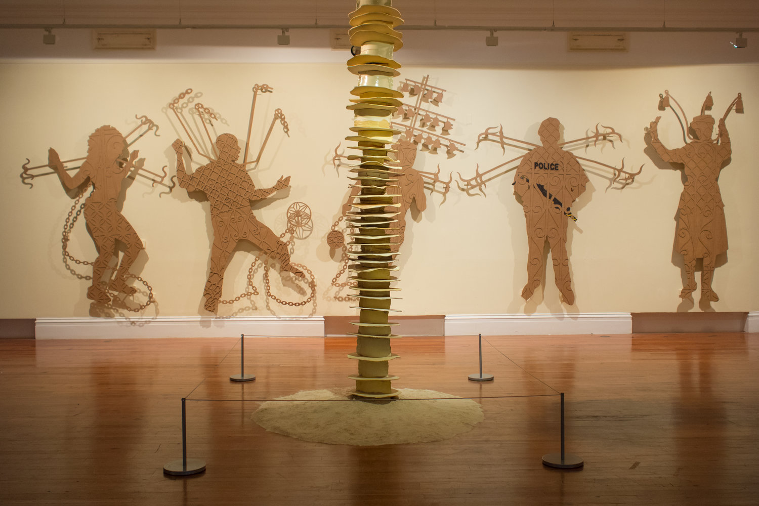 Brown figures are in high relief against the wall, each with items surrounding them. At the center are the layers of a pillar.