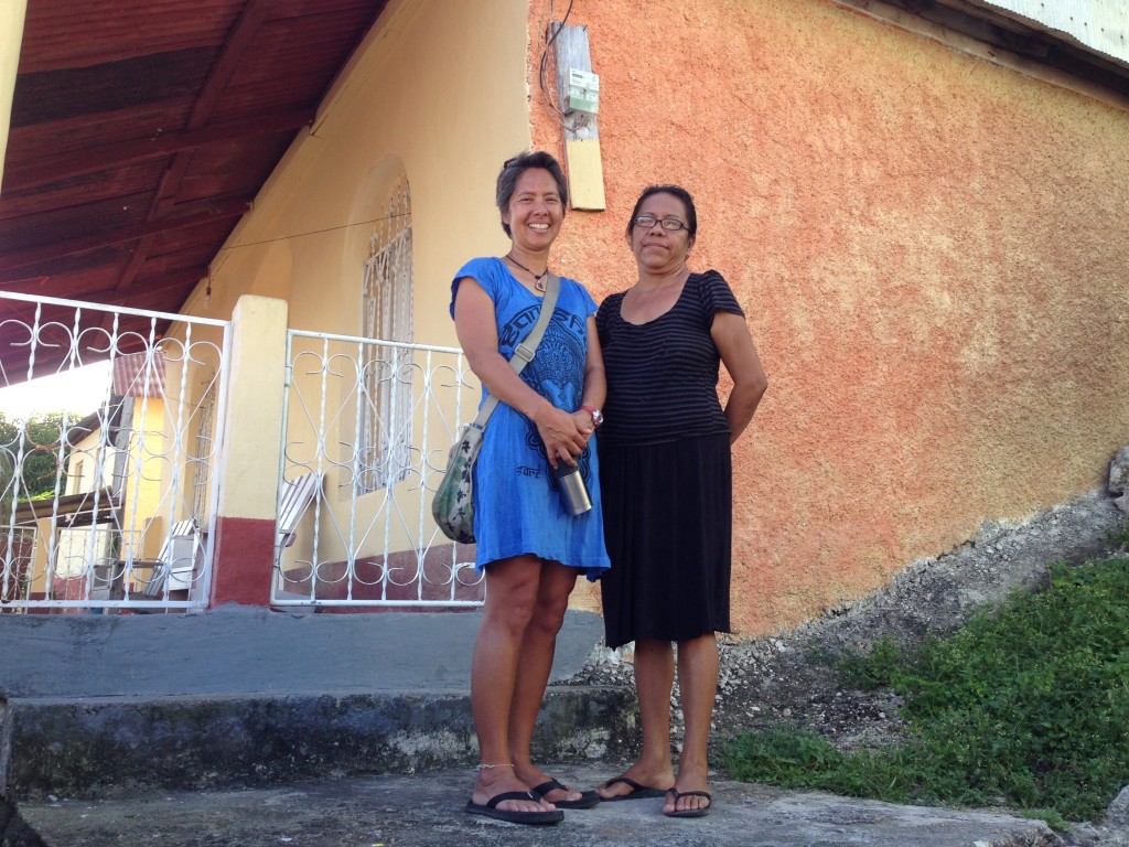 R standing in front of the house where she lived with the sister of the matriarch. The matriarch recently passed away.