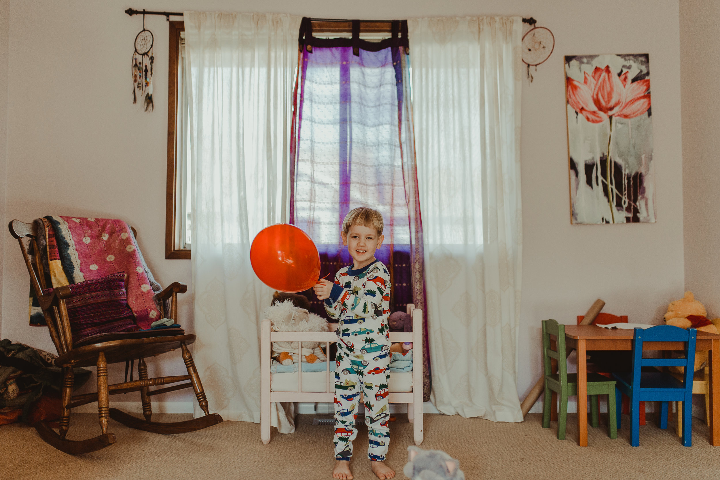  Toddler boy wearing pajamas playing with red balloon in Southern Oregon home. 