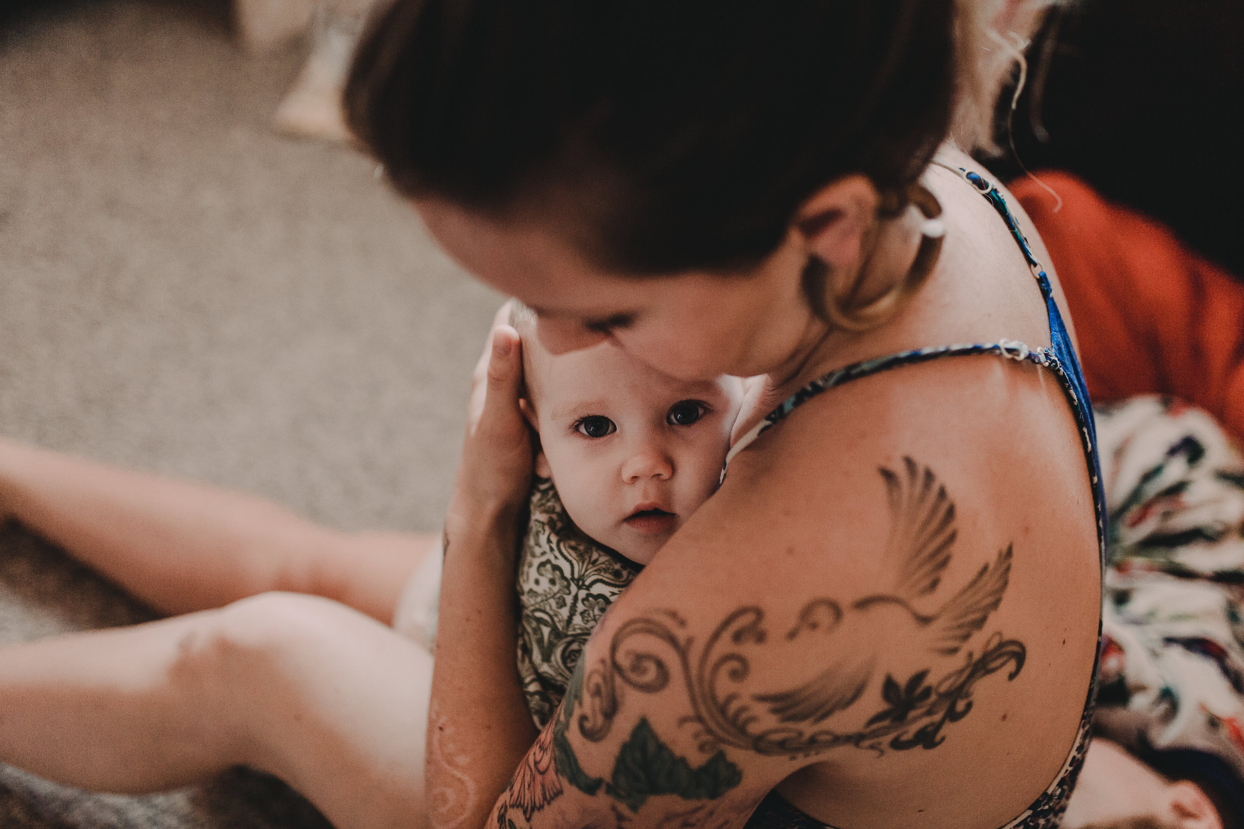  Tattooed Mother embracing baby girl who stares at the camera. 