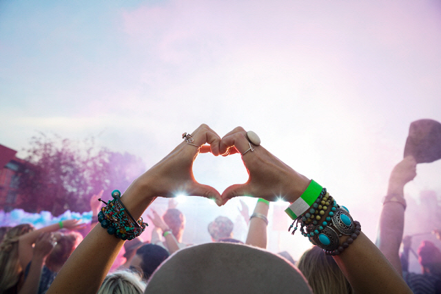 Woman forming heart-shape with hands in crowd at summer music festival
