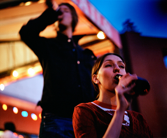 A young man and woman drink bottled beer outdoors