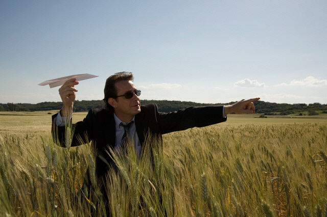 Businessman aiming paper plane in wheat field