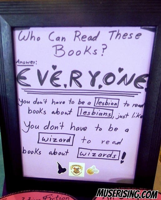 A handwritten sign that says: "Who can read these books? EVERYONE. You don't have to be a lesbian to read books about lesbians, just like you don't have to be a wizard to read books about wizards!"