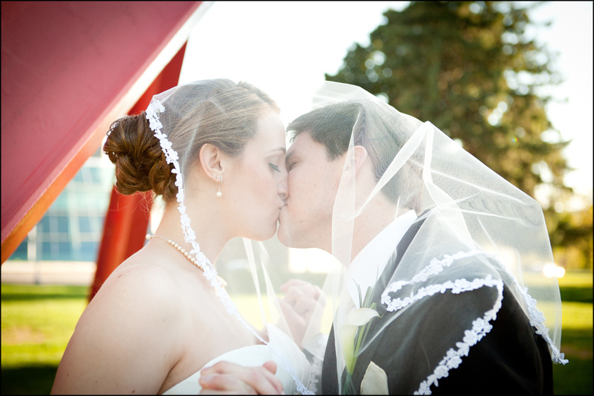 A bride's veil drapes over her groom's head too as they kiss at Muhlenberg College
