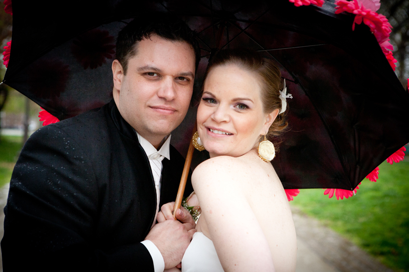 Bride and groom smile from under a black umbrella