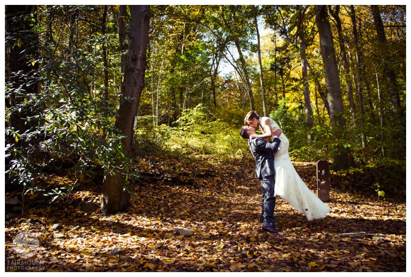 Groom lifts bride for kiss in woods in Fairmount Park
