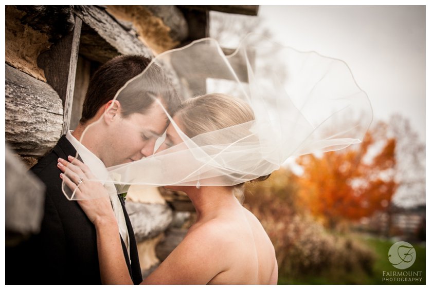veil covers bride and groom leaning against log cabin in Valley Forge Park in PA