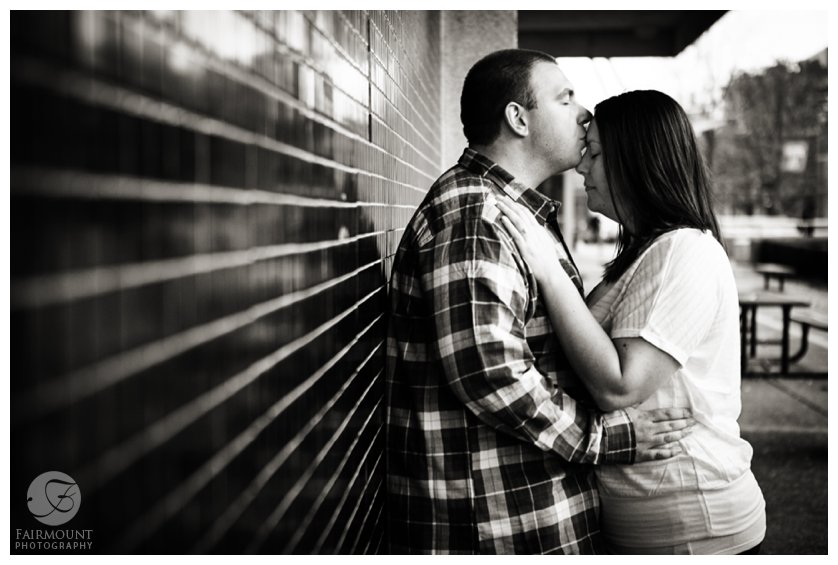 romantic portrait against black tile wall with guy kissing girl's forehead