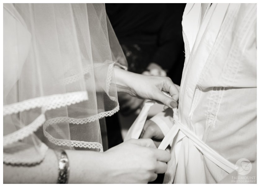 bride ties the belt of the kittel, a robe of white linen worn by the groom during the wedding ceremony