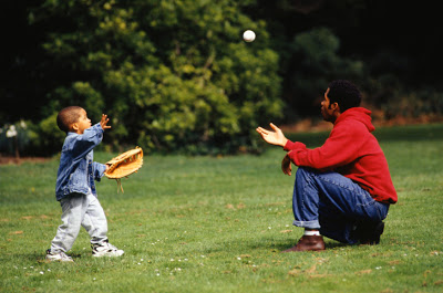 Father and son (3-4) playing catch in park, side view