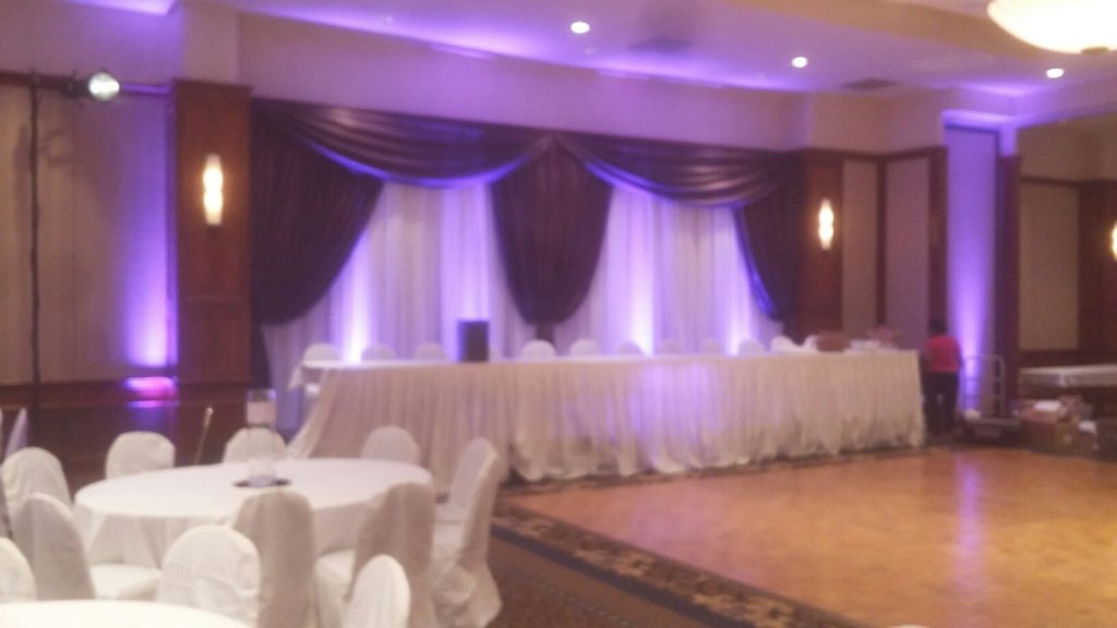 Picture of a wedding head table with AV for You uplights to illuminate the pipe and drape behind the table