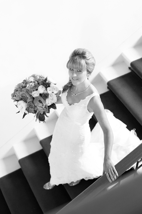 Bride on stairs holding bouquet, in a dress by Cymbeline