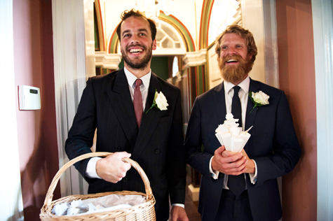 Two of the grooms men laughing, one holding confetti basket