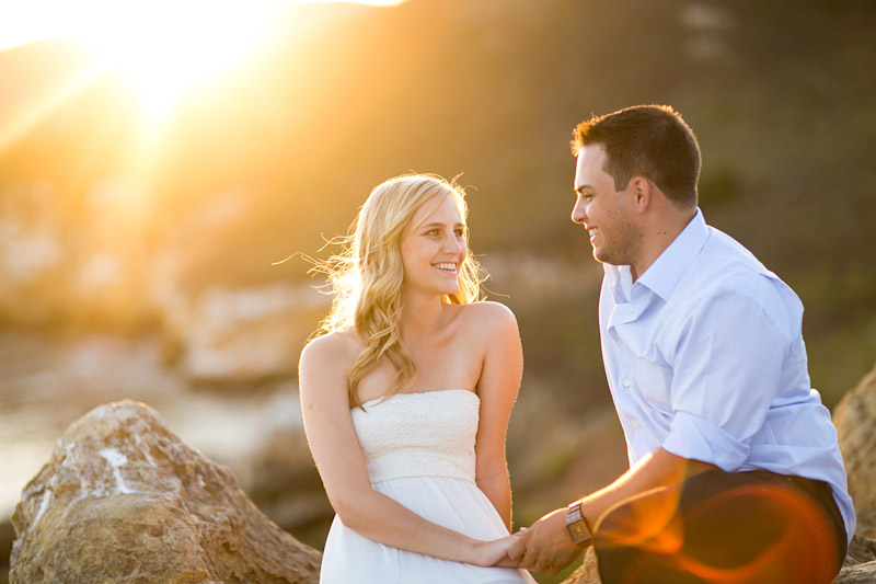 Avila Beach Engagement pictures of bride and groom holding sitting on rocks on the cliffs overlooking Avila Bay. 