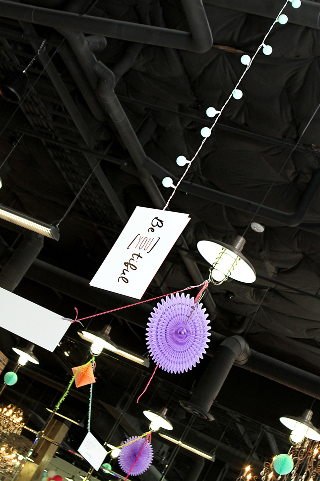 Cute watercolor sign hanging from rafters at a confetti party. So fun to hang them with bulb lights!