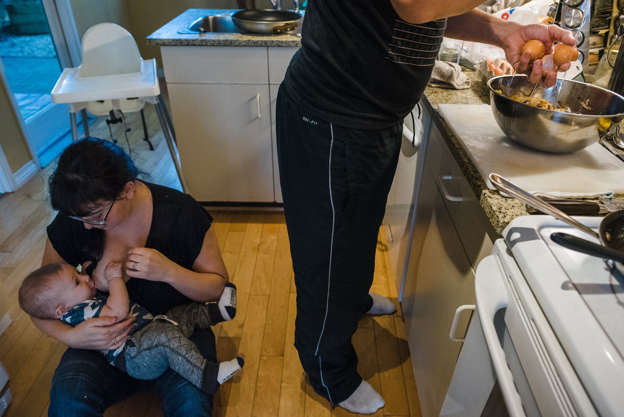 mom breastfeeding baby on the kitchen floor while dad is cooking