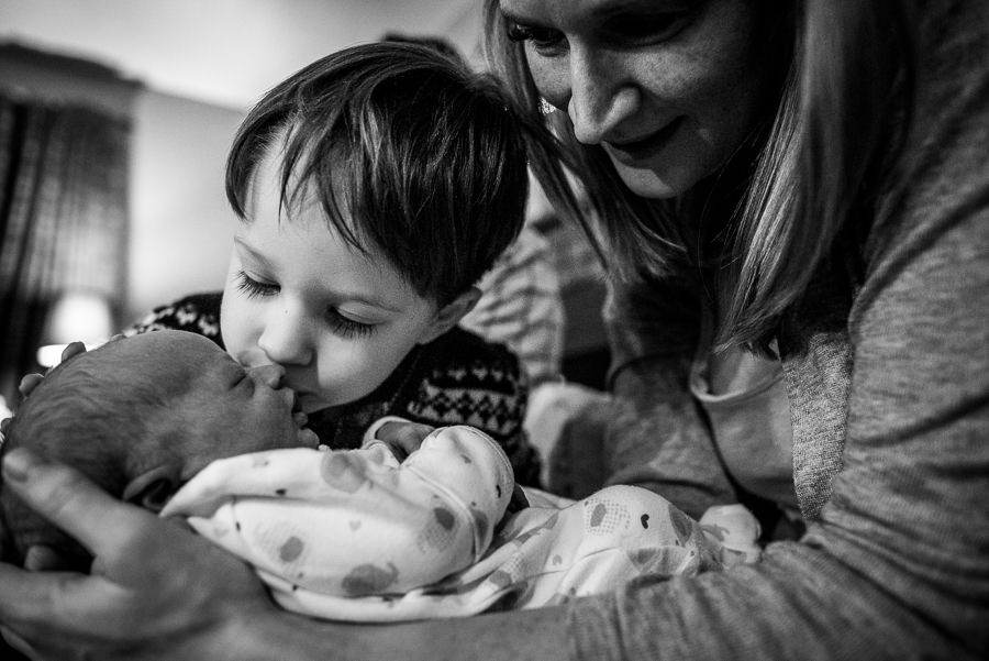 boy kissing his new baby brother while mom cuddles them both