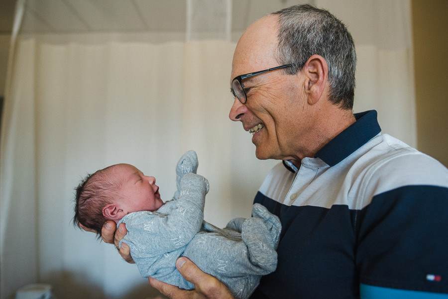 smiling grandfather holding newborn baby grandson 