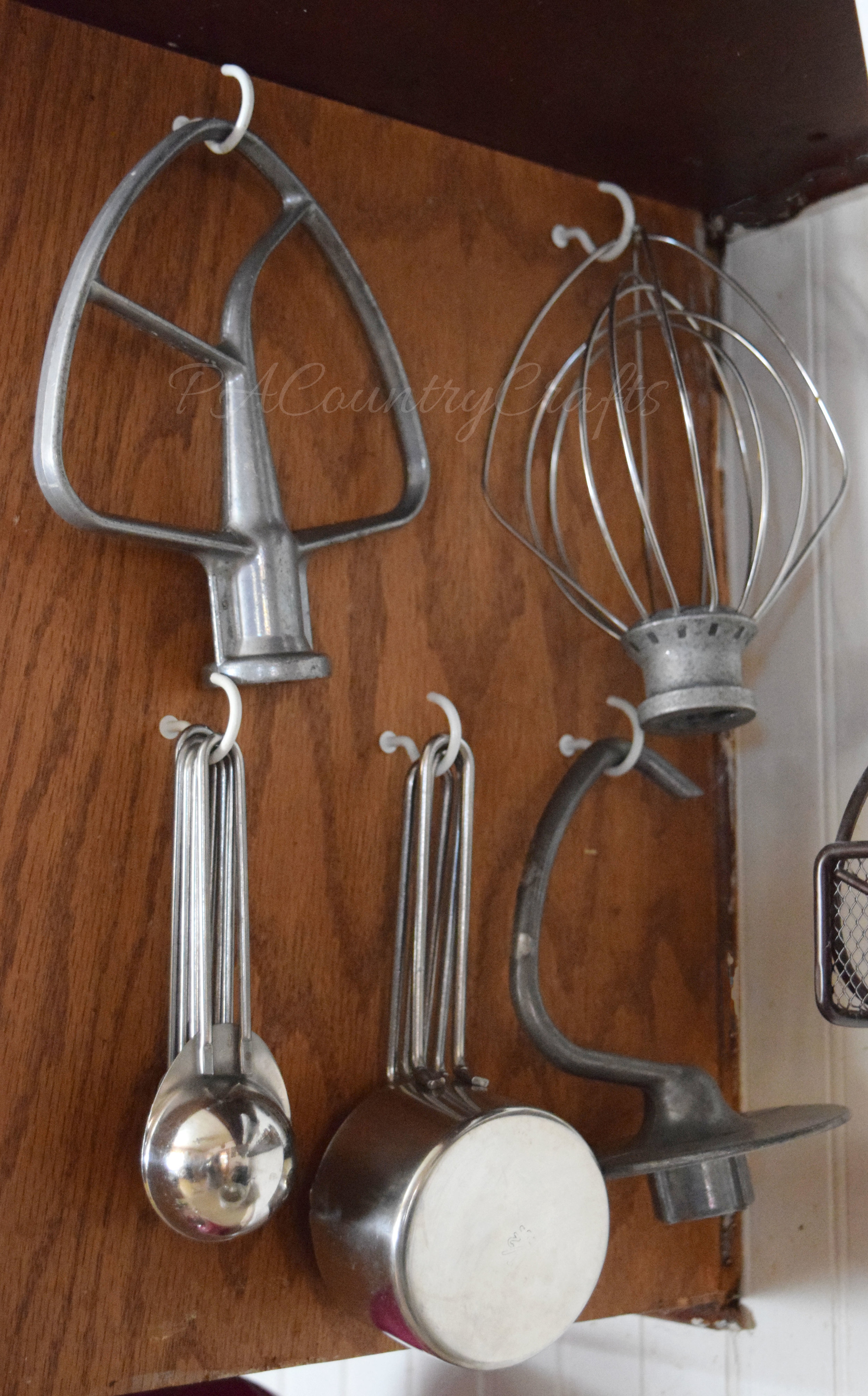 Hang mixer attachments and measuring cups from hooks on the side of a cupboard.