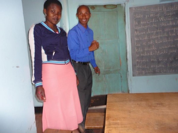 A man and woman stand in a classroom with the chalkboard behind them.