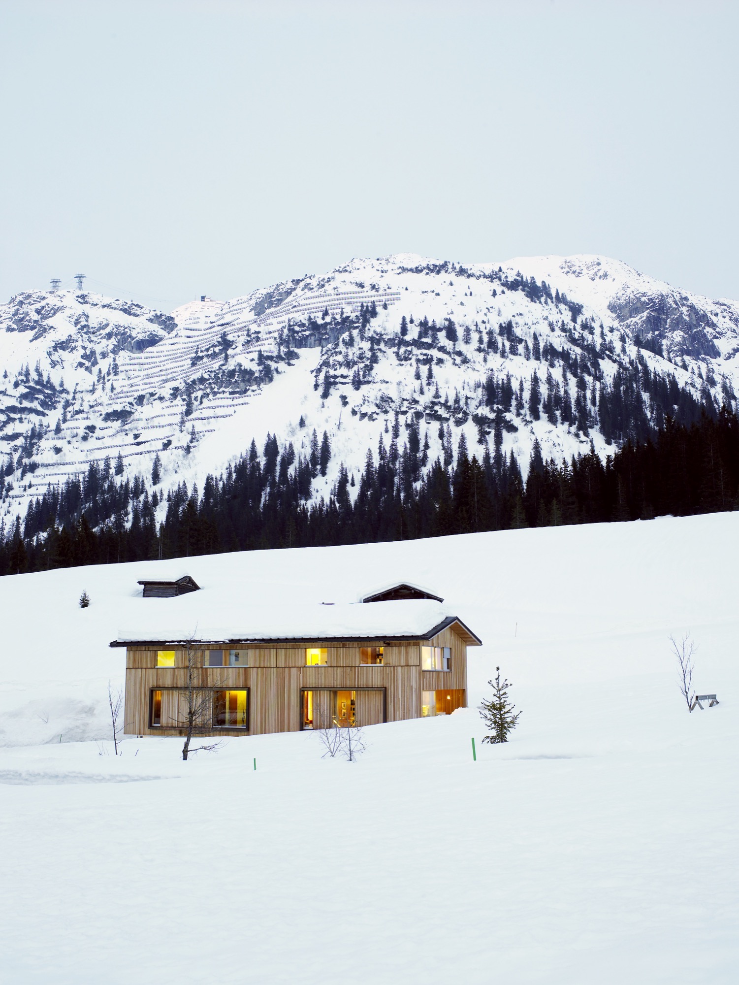 The Strolz House nestles in the winter snow at the edge of the Austrian village of Lech. Large wooden shutters help protect the windows against avalanche damage.