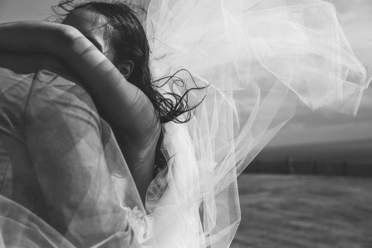 Black and White of Bride and Groom embracing, and veil blowing in the wind. 