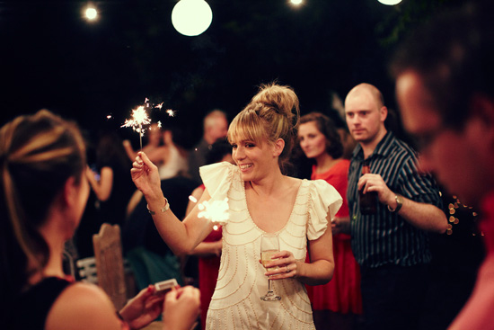Bride at engagament in white holding sparkler with guests around her