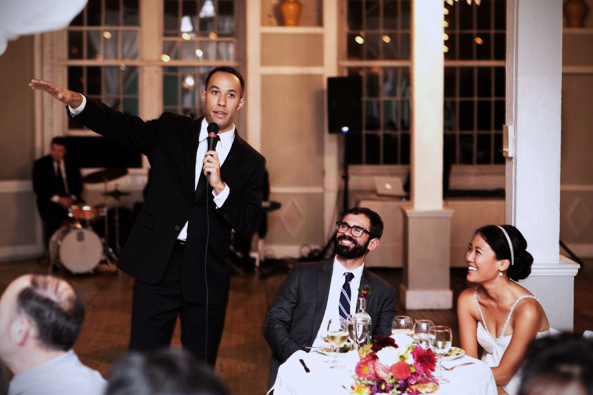 Man mcing a wedding with bride and groom sitting down smiling