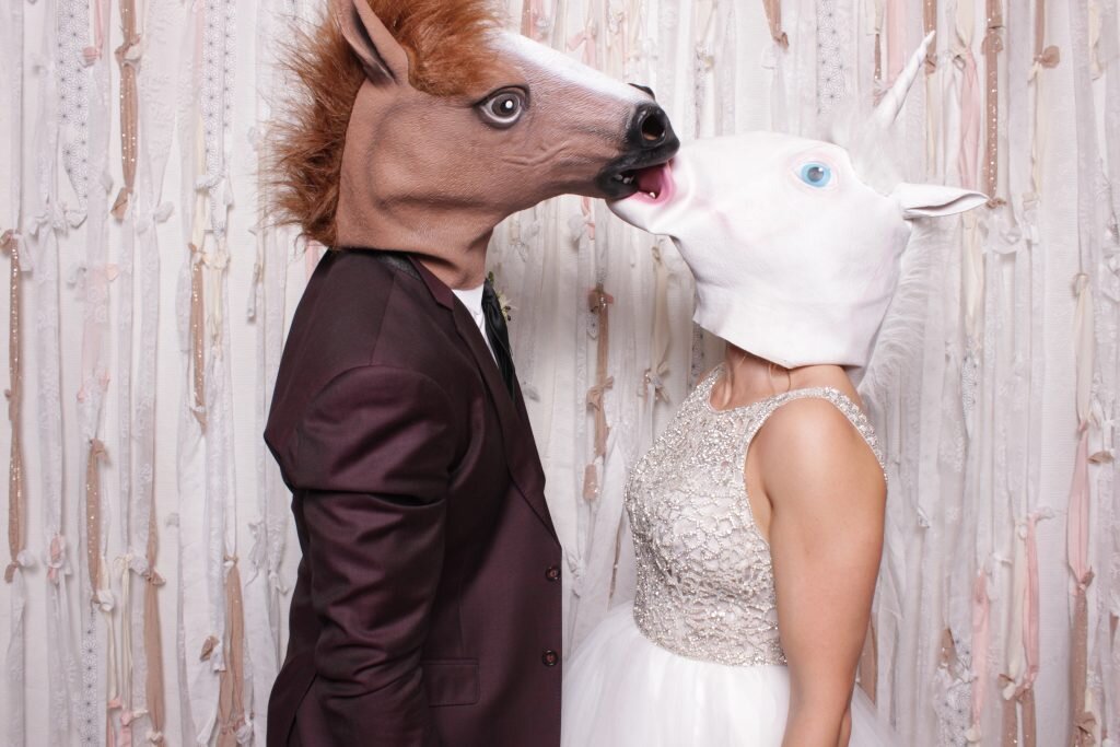 a bride and groom wear horse heads as props in a canmore photo booth