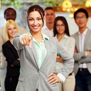 Smiling handsome businesswoman with team in office pointing finger at you