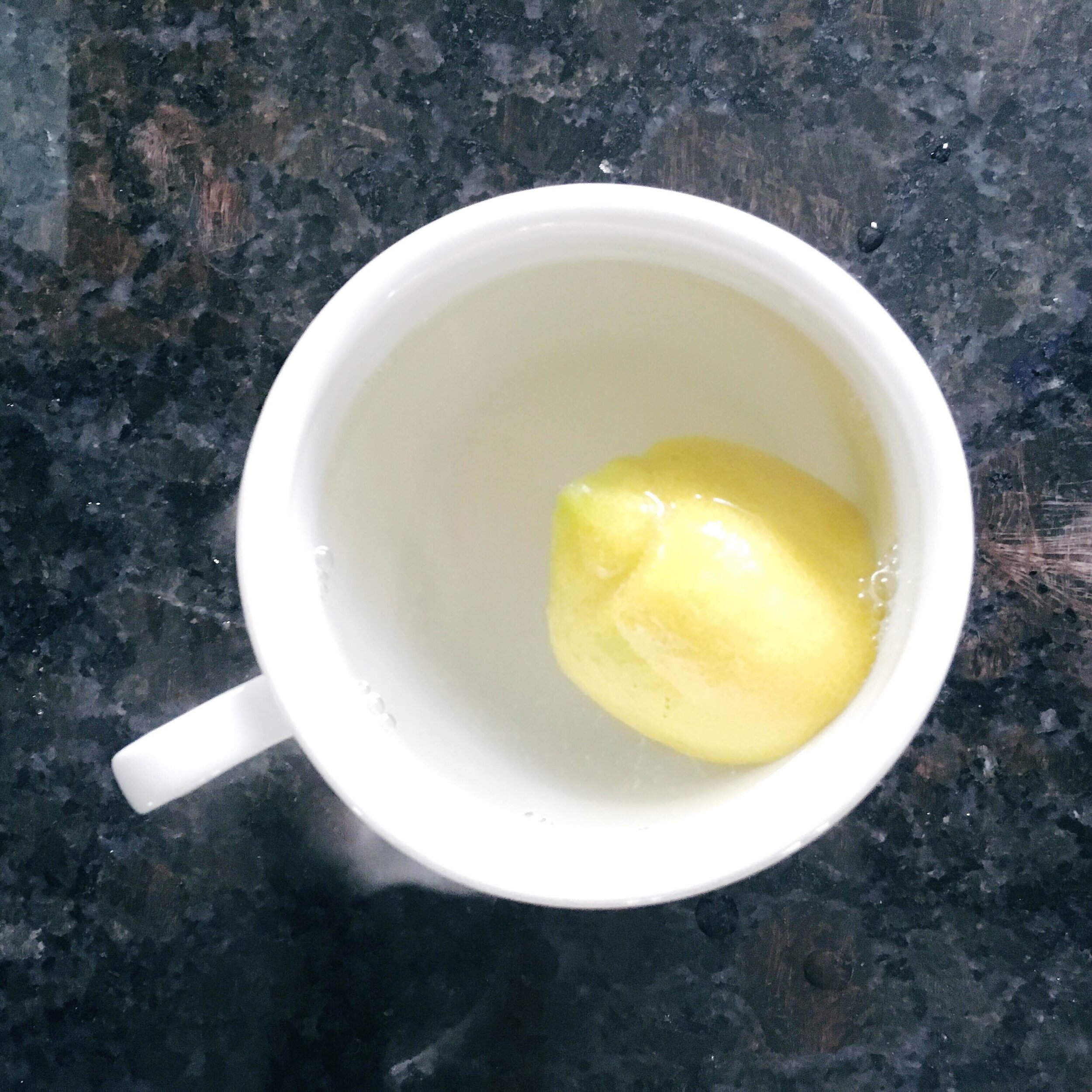 lemon half and hot water in white ceramic mug on dark granite counter