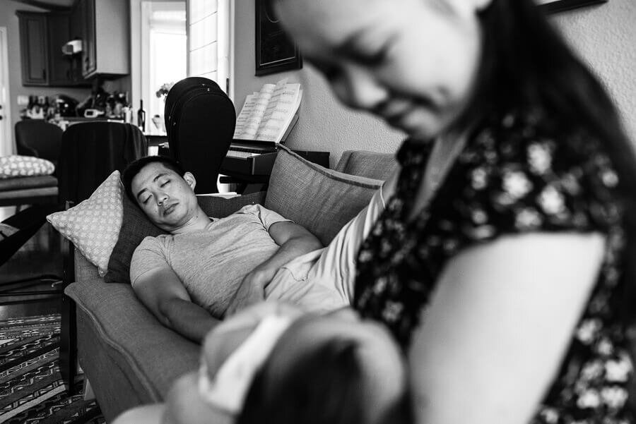 Dad sleeping on couch while mom holds baby