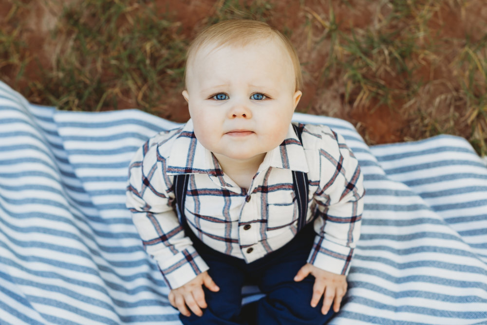  Baby brother sitting on picnic blanket looking up at the camera in stripes and suspenders #tealawardphotography #texasfamilyphotographer #amarillophotographer #amarillofamilyphotographer #lifestylephotography #emotionalphotography #familyphotosoot #family #lovingsiblings #purejoy #familyphotos #familyphotographer #greatoutdoors 