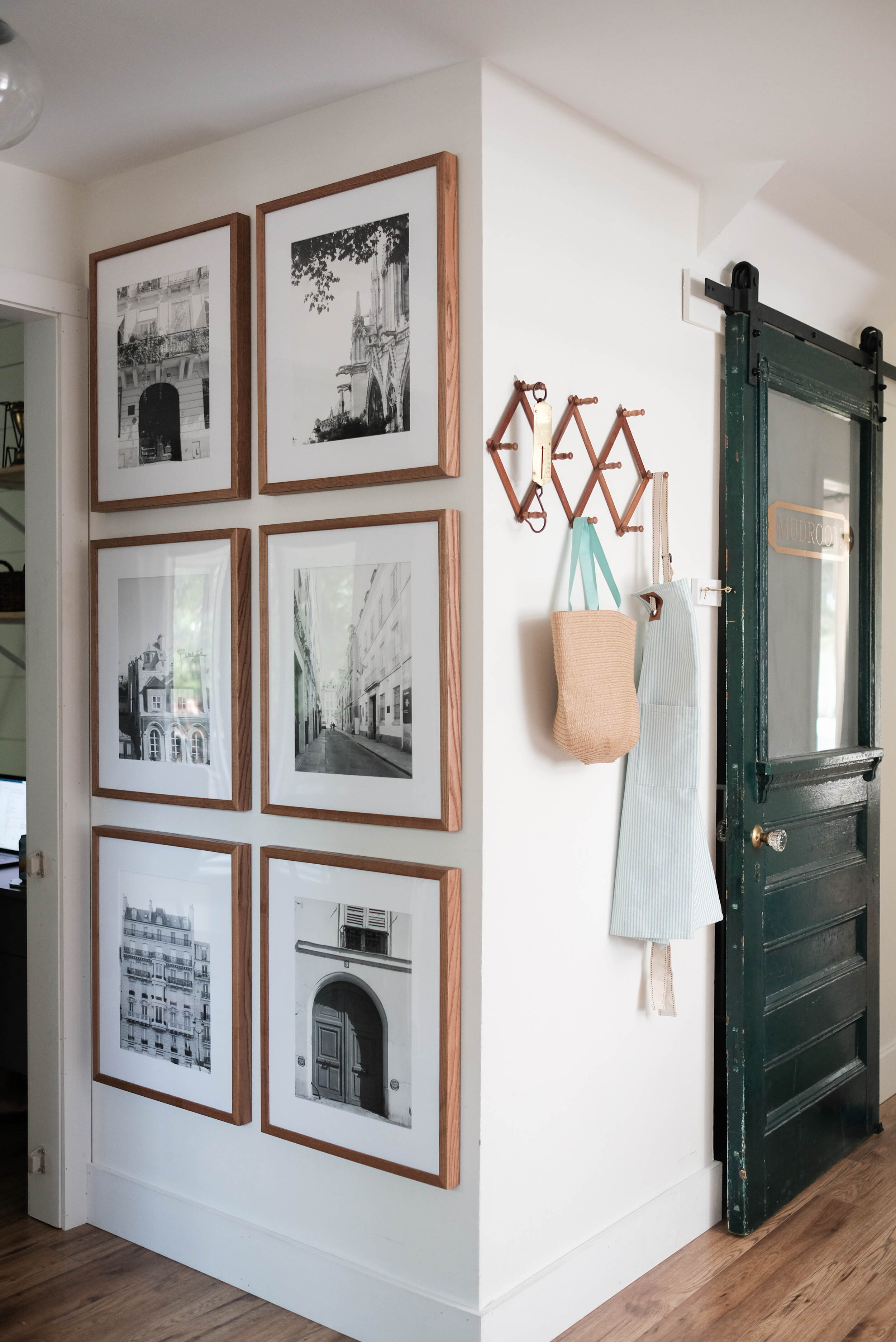 Symmetrical gallery wall in a hallway with light walnut frames from PosterJack. Green barn door to the right with a wooden accordion hook