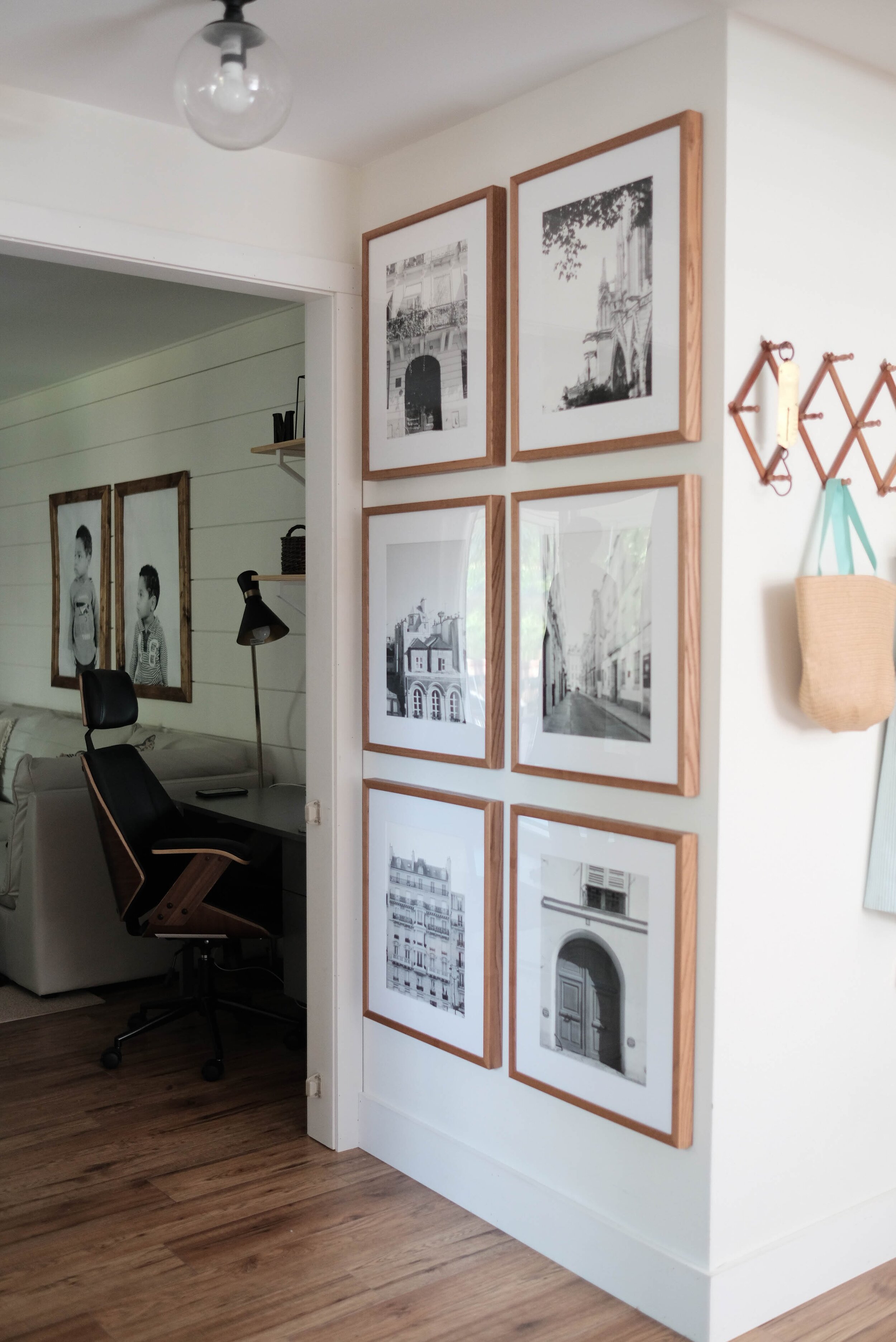 Symmetrical gallery wall in a hallway with light walnut frames from PosterJack. Wood accordion hook to the right and living room with a desk and office chair to the left.